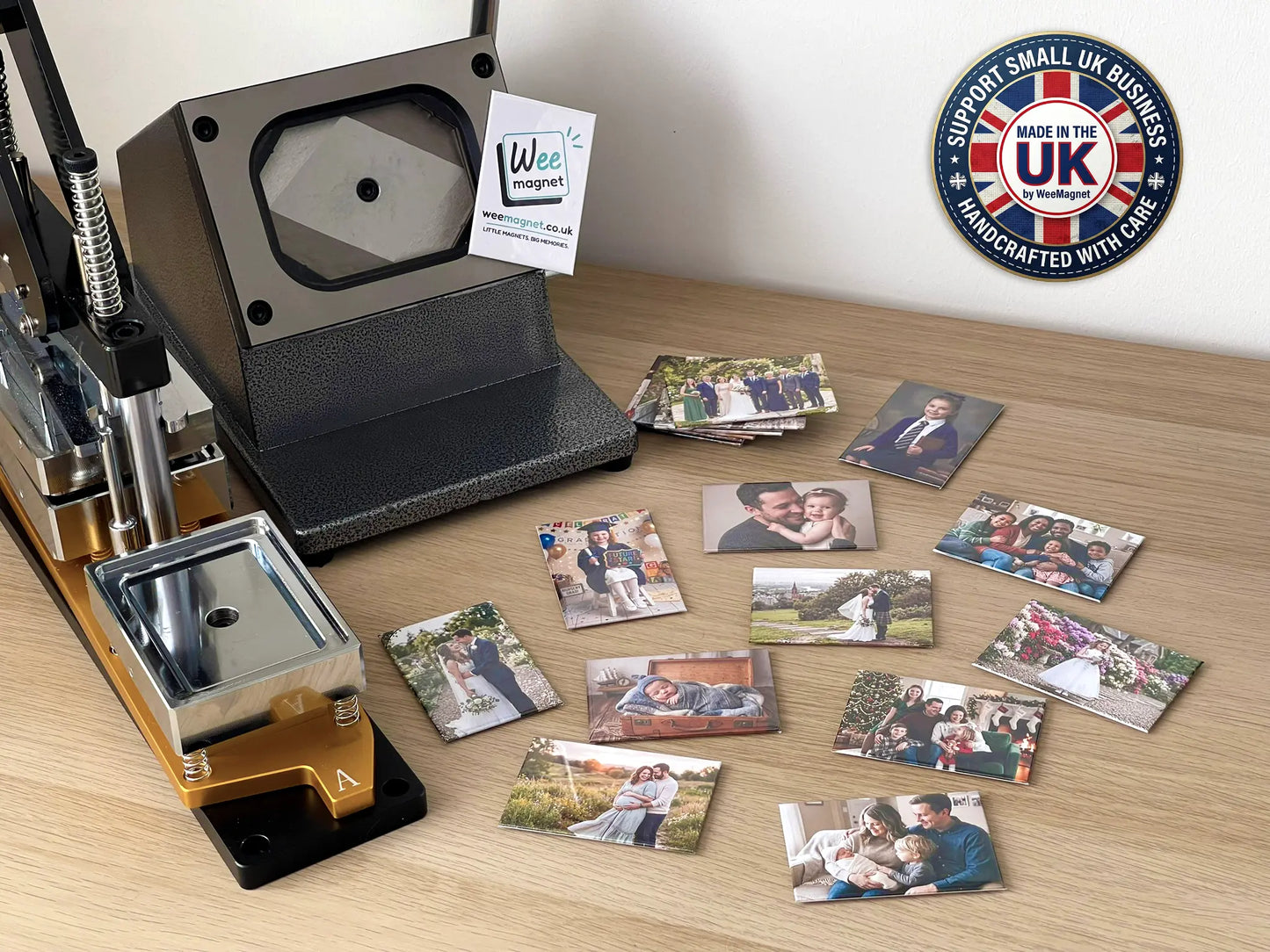 A heavy-duty magnet press machine sitting on a wooden desk next to a collection of finished Wee Magnet custom photo magnets and a Made in the UK support small business badge.