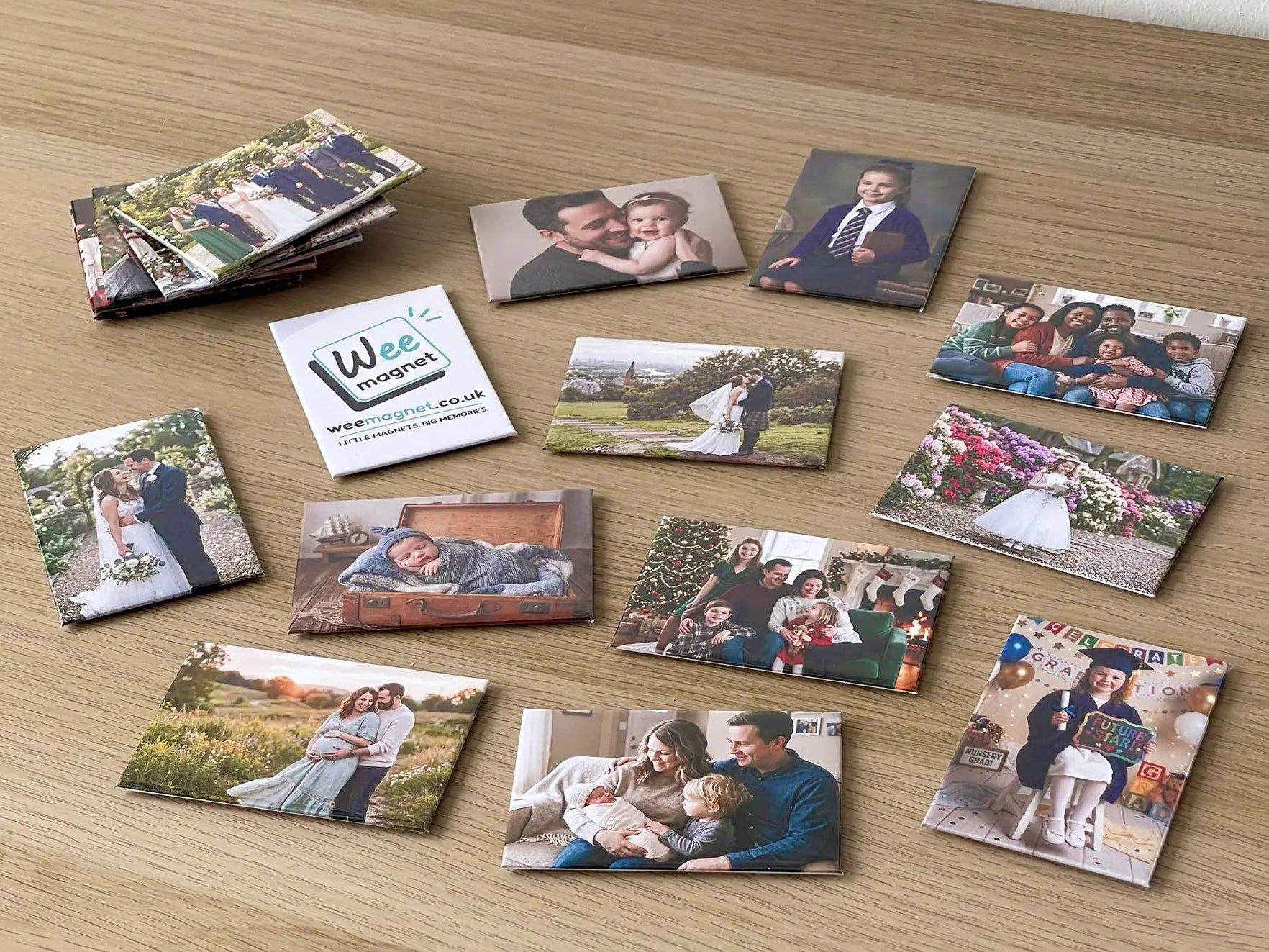 A wide variety of personalized Wee Magnet photo magnets scattered on a wooden table, featuring family portraits, newborn babies, weddings, and graduations.
