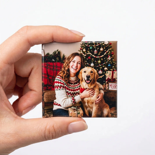 A hand holding up a high-quality square custom photo magnet showing a smiling woman sitting next to her golden retriever dog in front of a decorated Christmas tree.