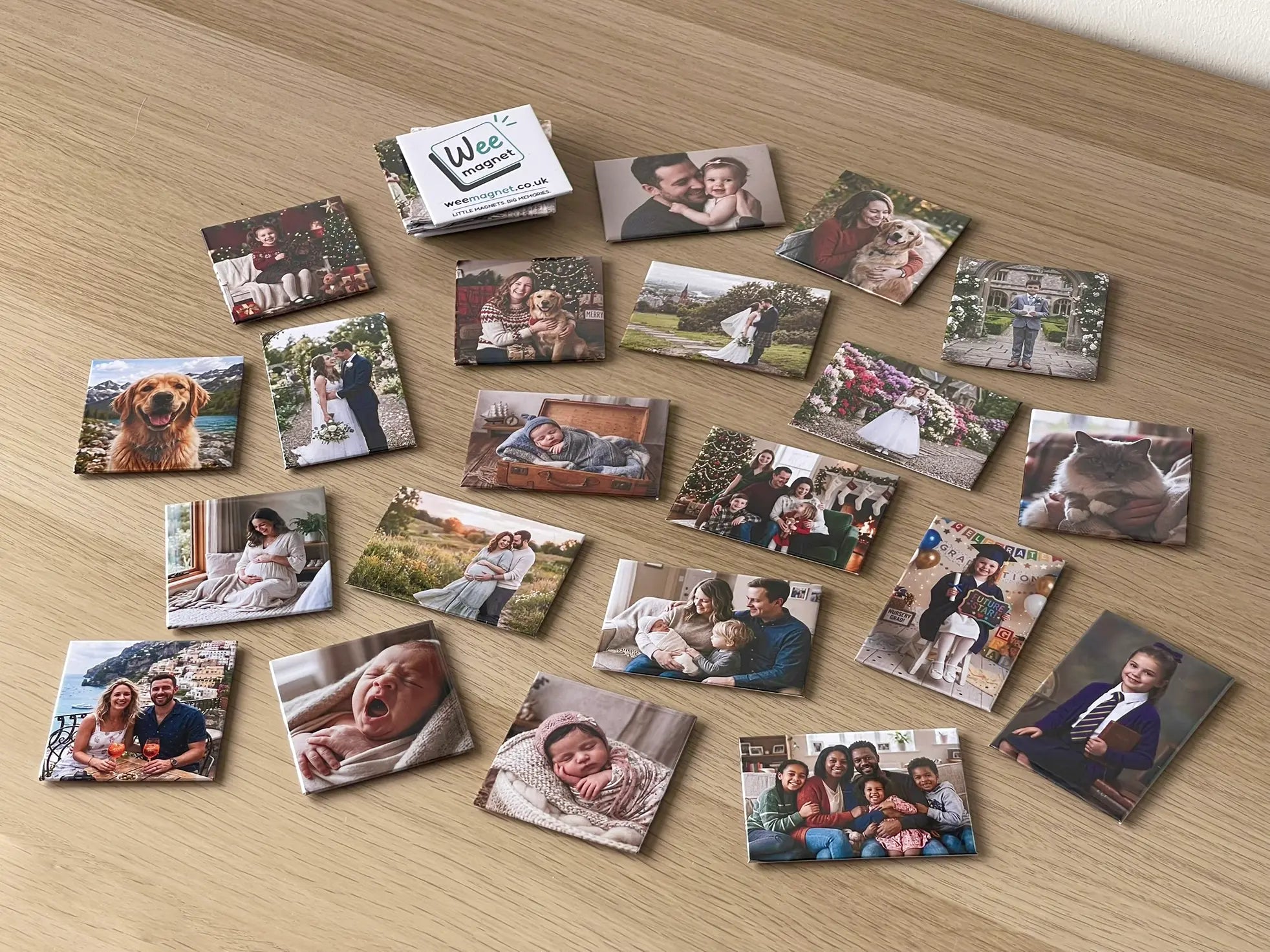 A wide collection of premium personalised photo fridge magnets scattered across a wooden table. The custom magnets showcase a variety of treasured memories, including family portraits, maternity photoshoots, newborn babies, weddings, and pets, alongside a Wee Magnet branded magnet.